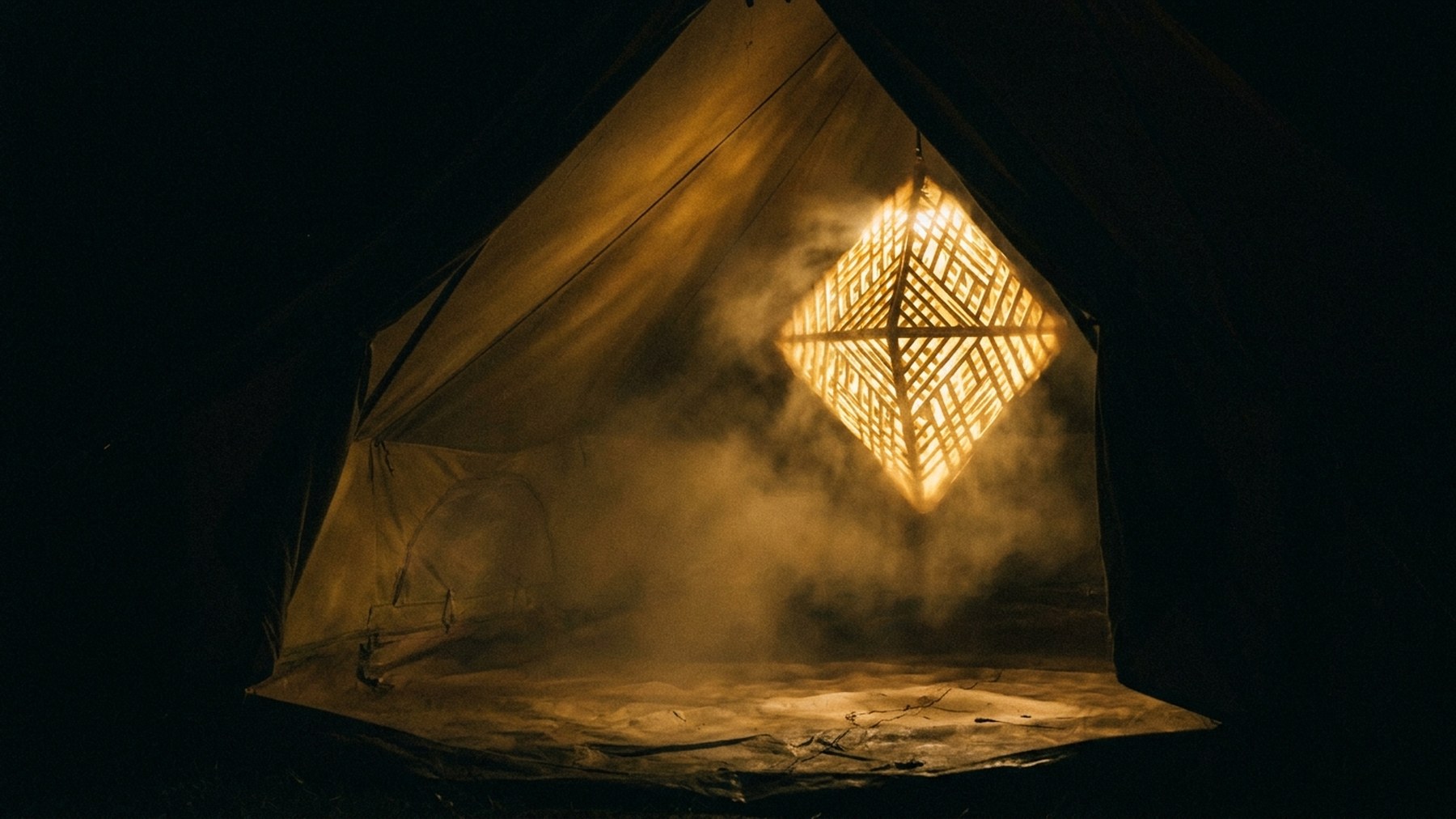 En lysende geometrisk rude svæver i et telt og kaster gyldent lys på dugen