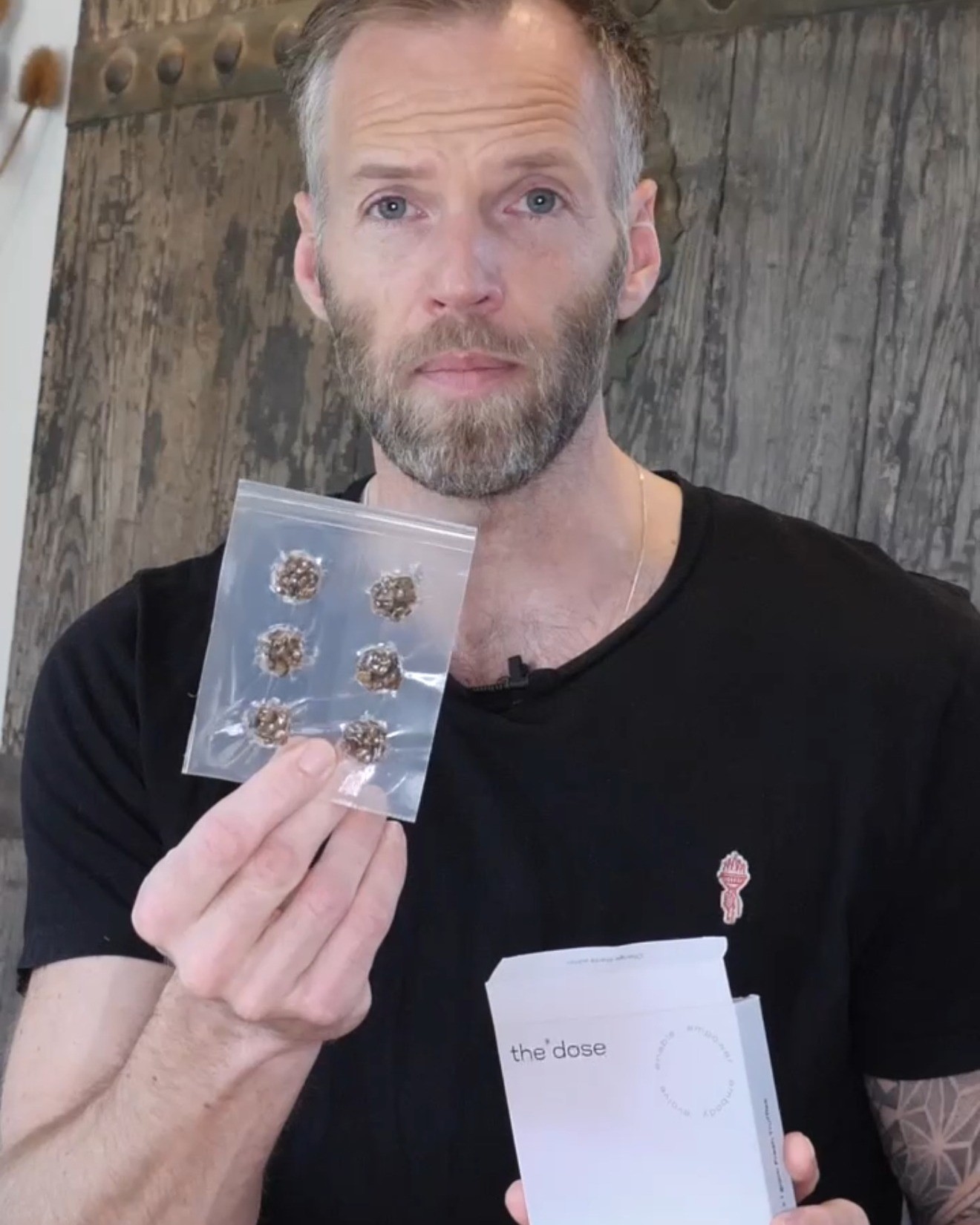 Asger foran en gammel trædør med en pose mikrodoser i den ene hånd og the*dose-æsken i den anden