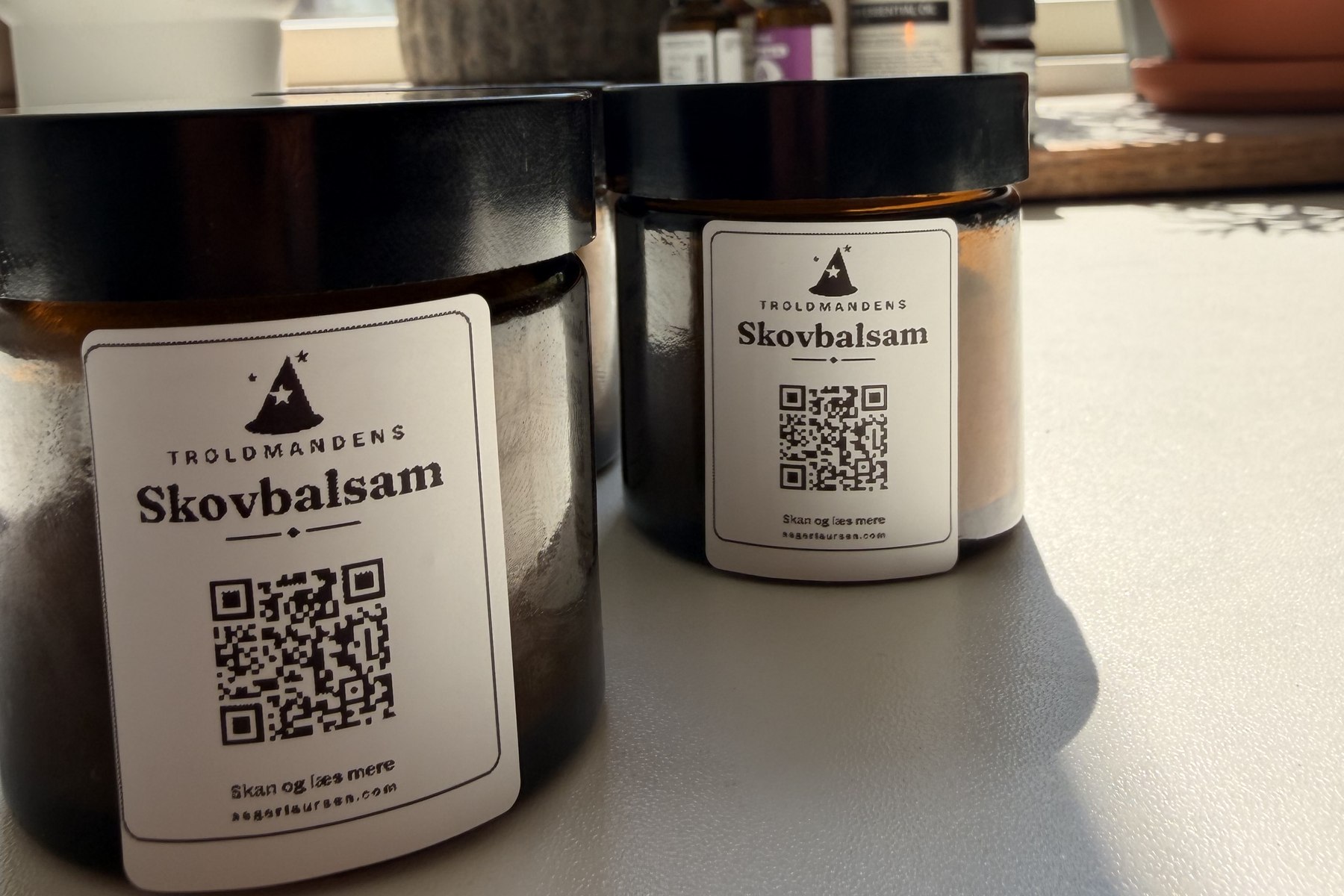 To brune glaskrukker med etiketten Troldmandens Skovbalsam, på vindueskarmen mellem urterne
